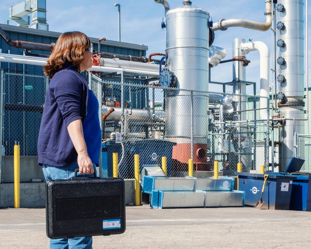 Woman with testing equipment outside a petrochemical facility.